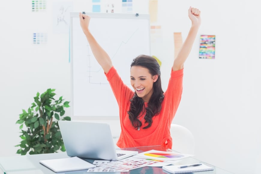 Excited woman raising her arms while working on her laptop in her office.jpeg